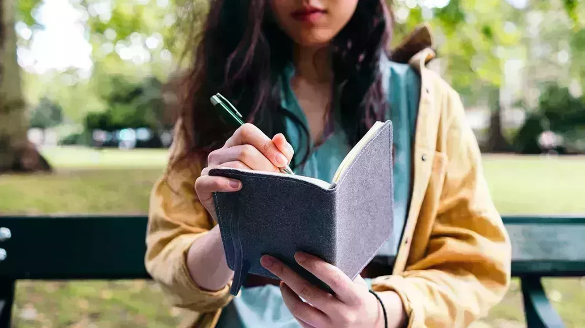 Person sitting on bench in park writes in small notebook 1
