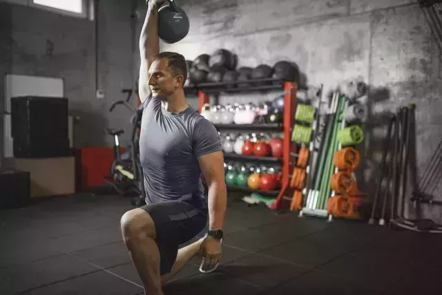 mid adult man practicing walking lunge with kettlebell during cross training in the gym