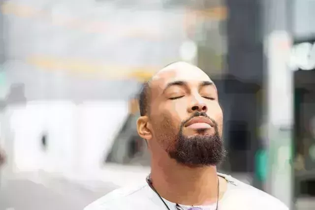 a handsome man standing outside with his eyes closed, enjoying a moment of peace