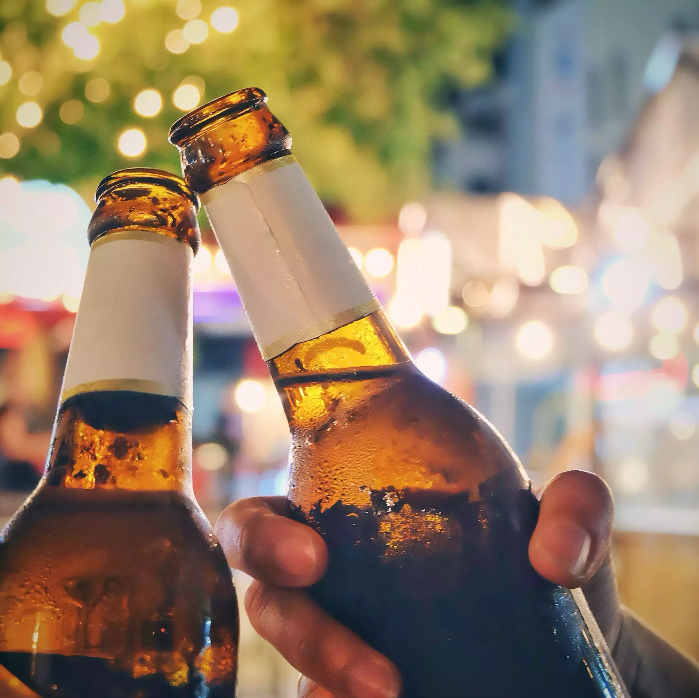 Close-Up Of Friends Toasting Beer Bottles At Night