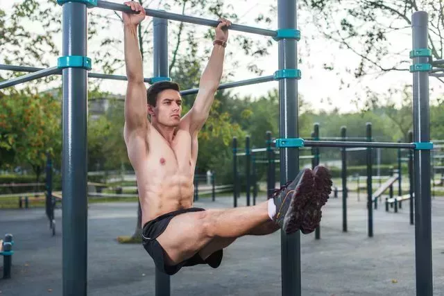 young fitness man doing hanging leg raises exercise working out his abs in the park