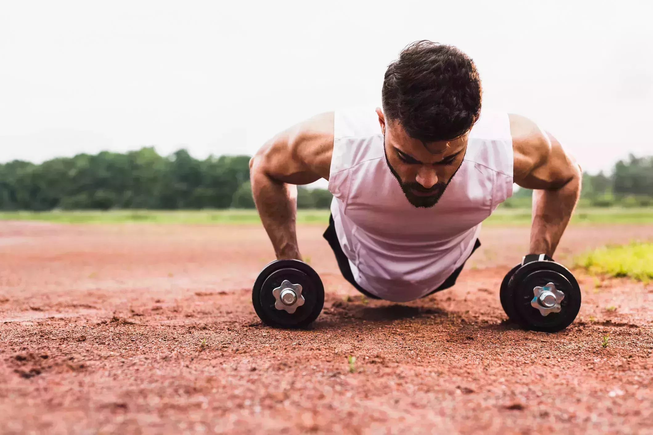 athlete doing pushups with dumbbells on sports field