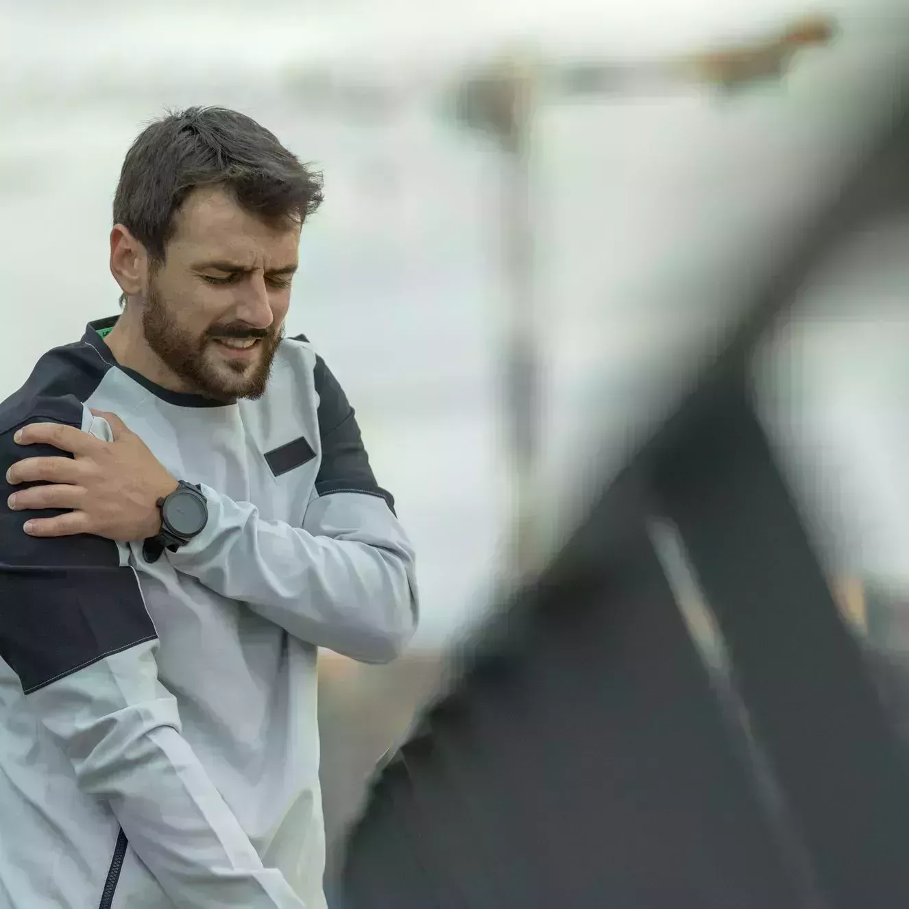 sportsman has pain in his shoulder during a relaxation exercise near the river bank handsome young athlete in sports suit is having a shoulder injury during morning running in the city