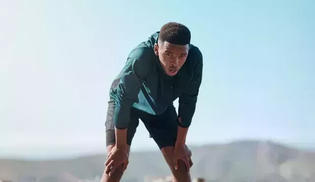 cropped portrait of a handsome young man hunched over and catching his breathe after running outdoors