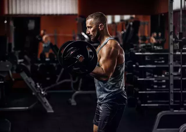 man doing biceps lifting barbell in a gym