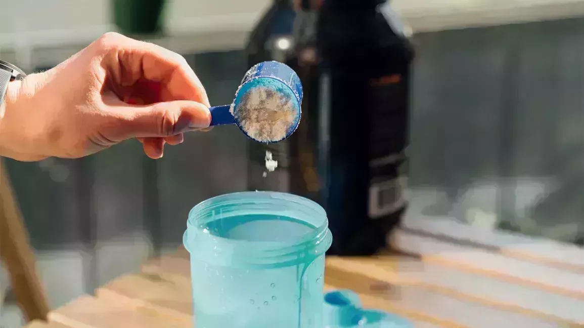 person pouring protein powder into a blue bottle