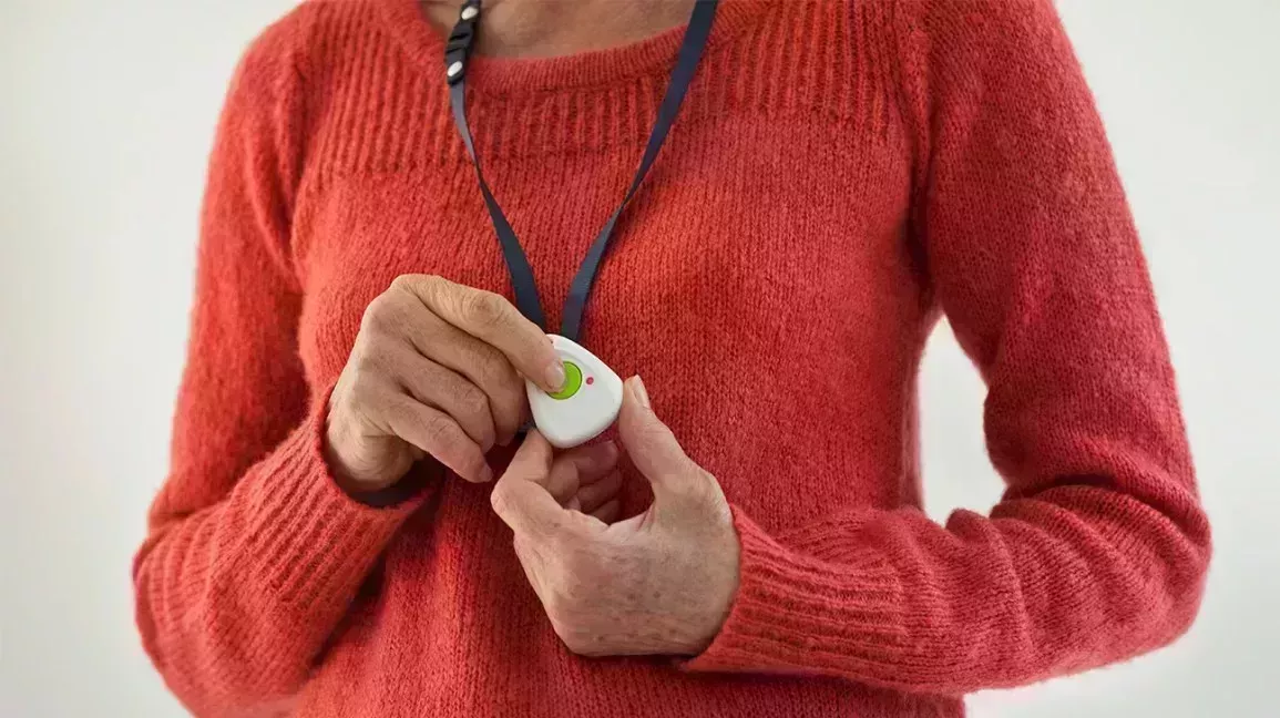 older person pressing help button on medical alert device