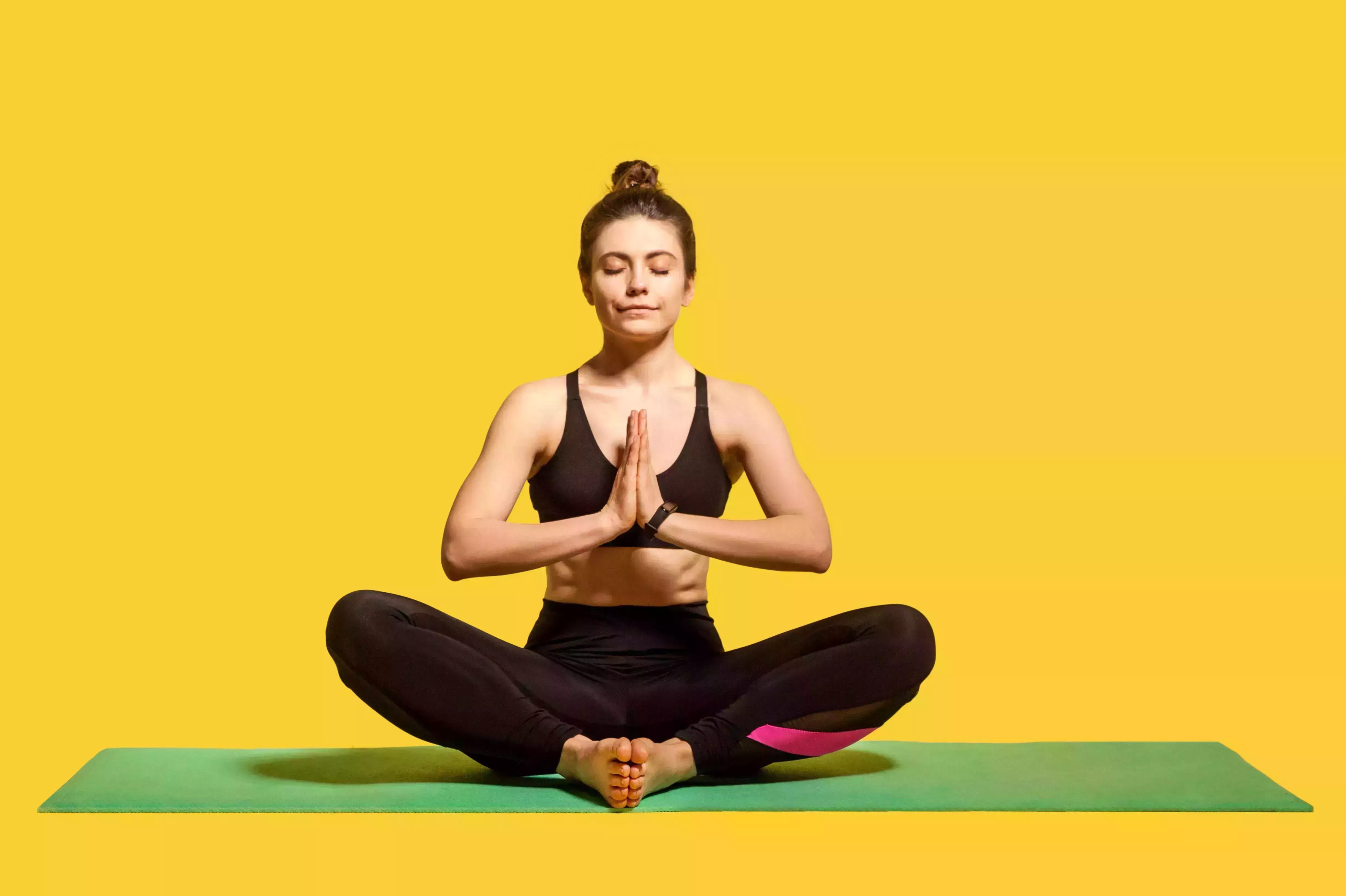 concentrated peaceful woman with hair bun in tight sportswear sitting on mat practicing yoga, holding hands in namaste