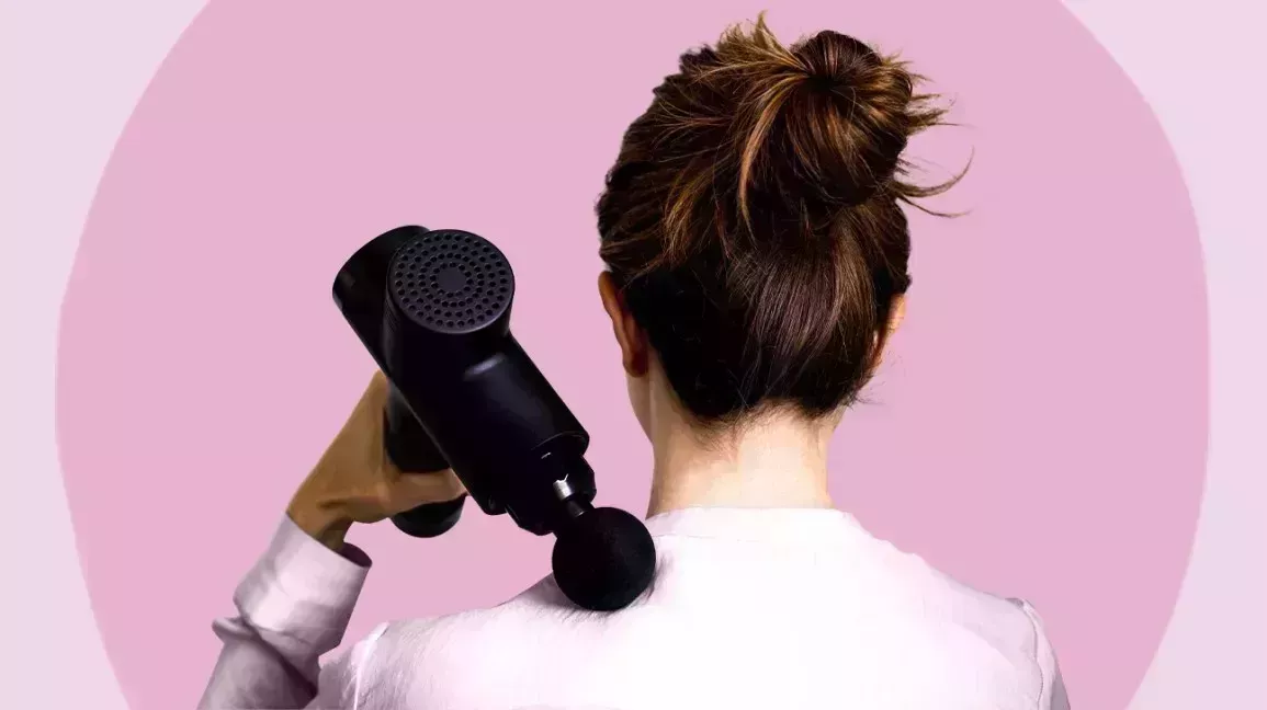 Woman using a massage gun on her shoulder