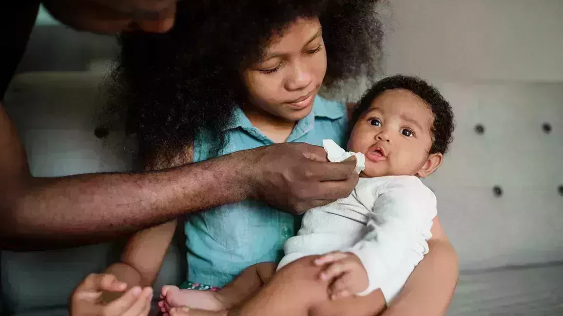 baby with mouth ulcers being held by a sibling