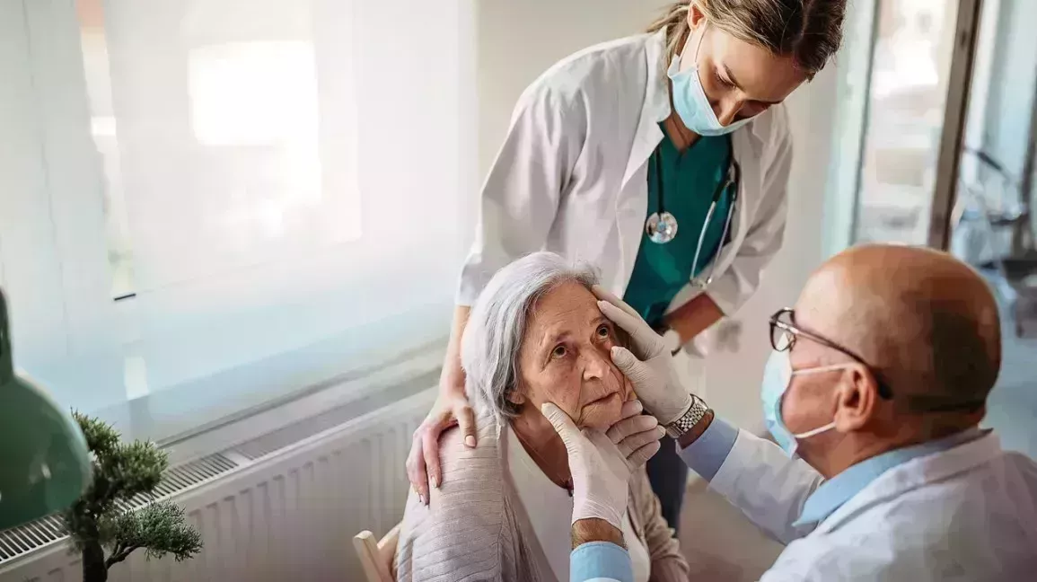 an elderly woman gets her eyes checked for glaucoma by an eye doctor with a nurse next to her