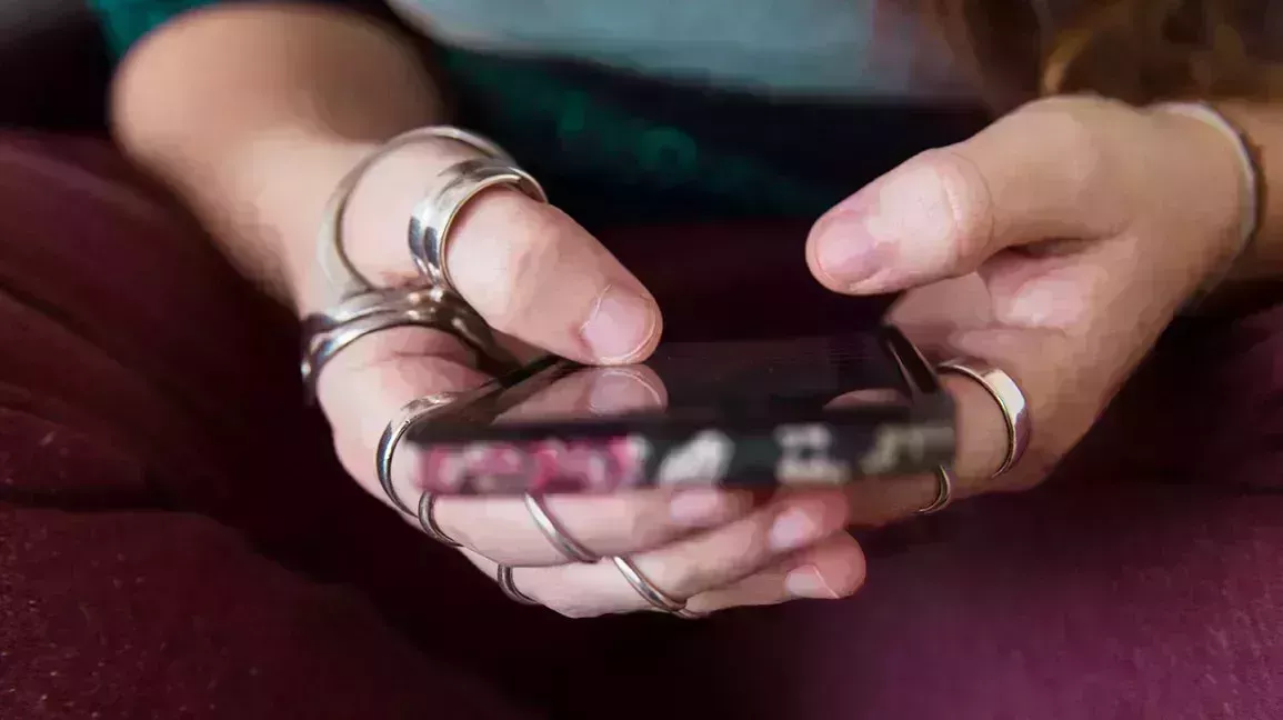 A person wearing ring splints holding a cell phone.