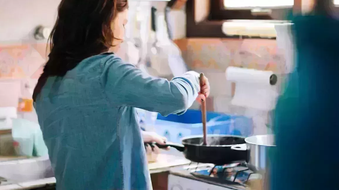 Person stirring food in a skillet held over a gas stovetop.