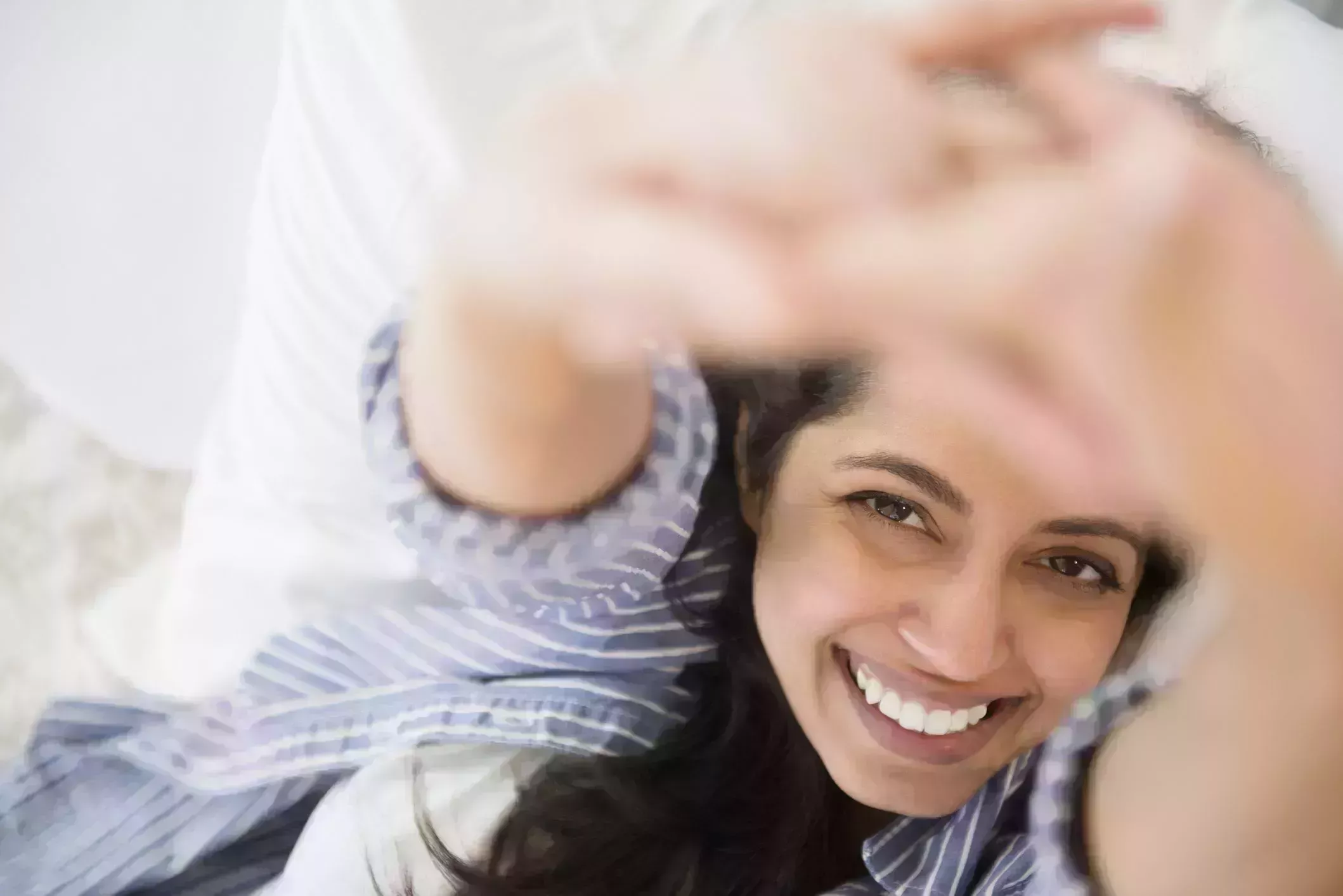 morning stretches – Close up portrait of smiling Asian woman laying in bed morning stretches – close up portrait of smiling asian woman laying in bed with fingers interlaced and arms stretched