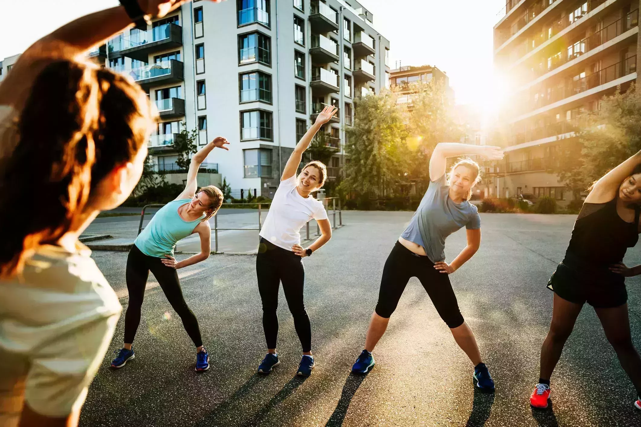 morning stretches – Urban Fitness Group Warming Up For Run morning stretches – four women being led by another doing side stretch outside