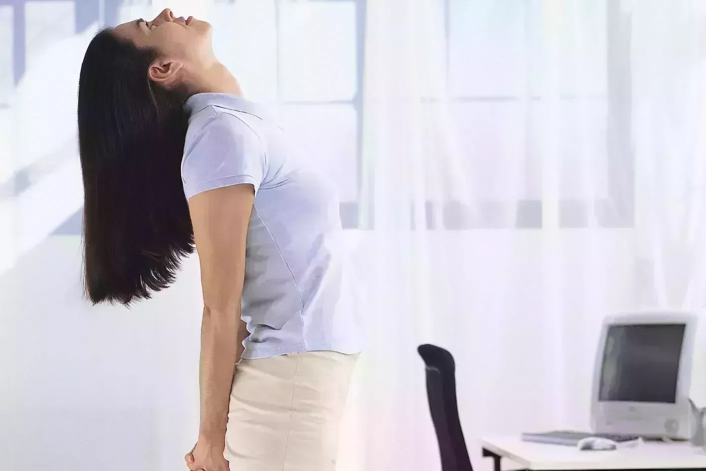 morning stretches – Woman stretching morning stretches – woman standing beside her desk doing chest opener stretch