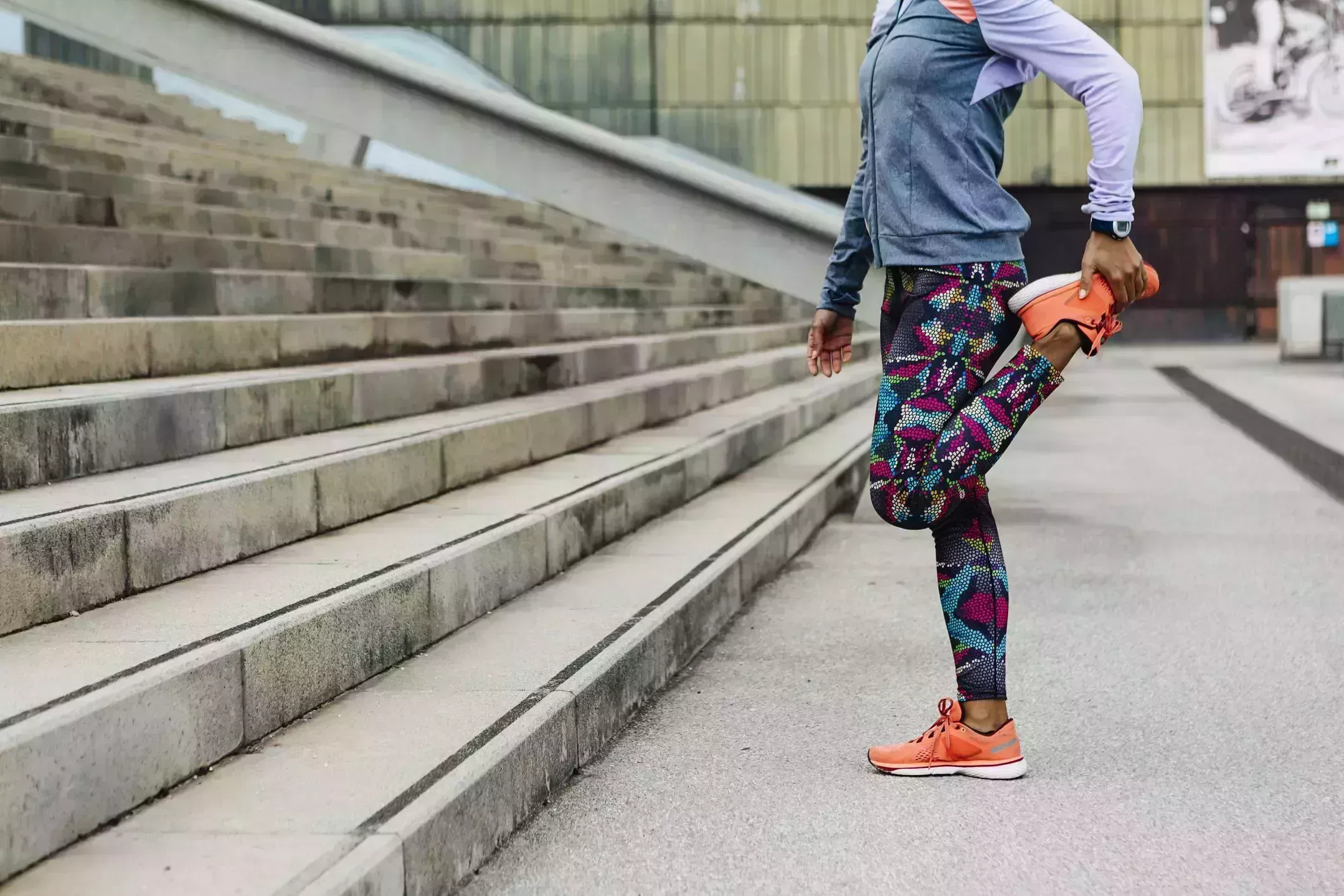 morning stretches – Athletic woman n workout clothes stretching legs before running morning stretches – woman standing in front of outdoor stairs in workout clothes doing a quad stretch