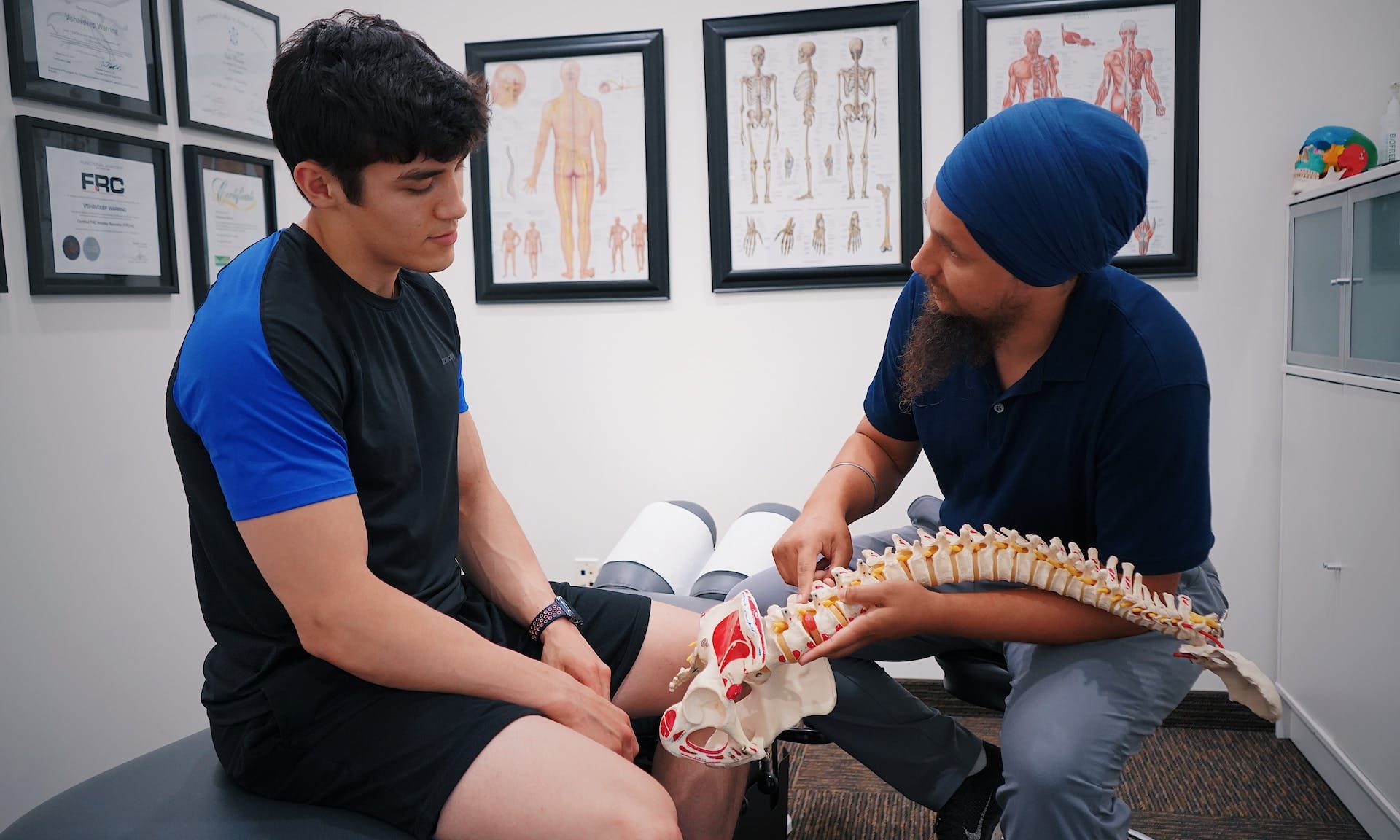 Doctor o profesional de la salud discutiendo la salud ósea y mostrando un modelo de columna vertebral a un paciente sentado en una cama en la oficina