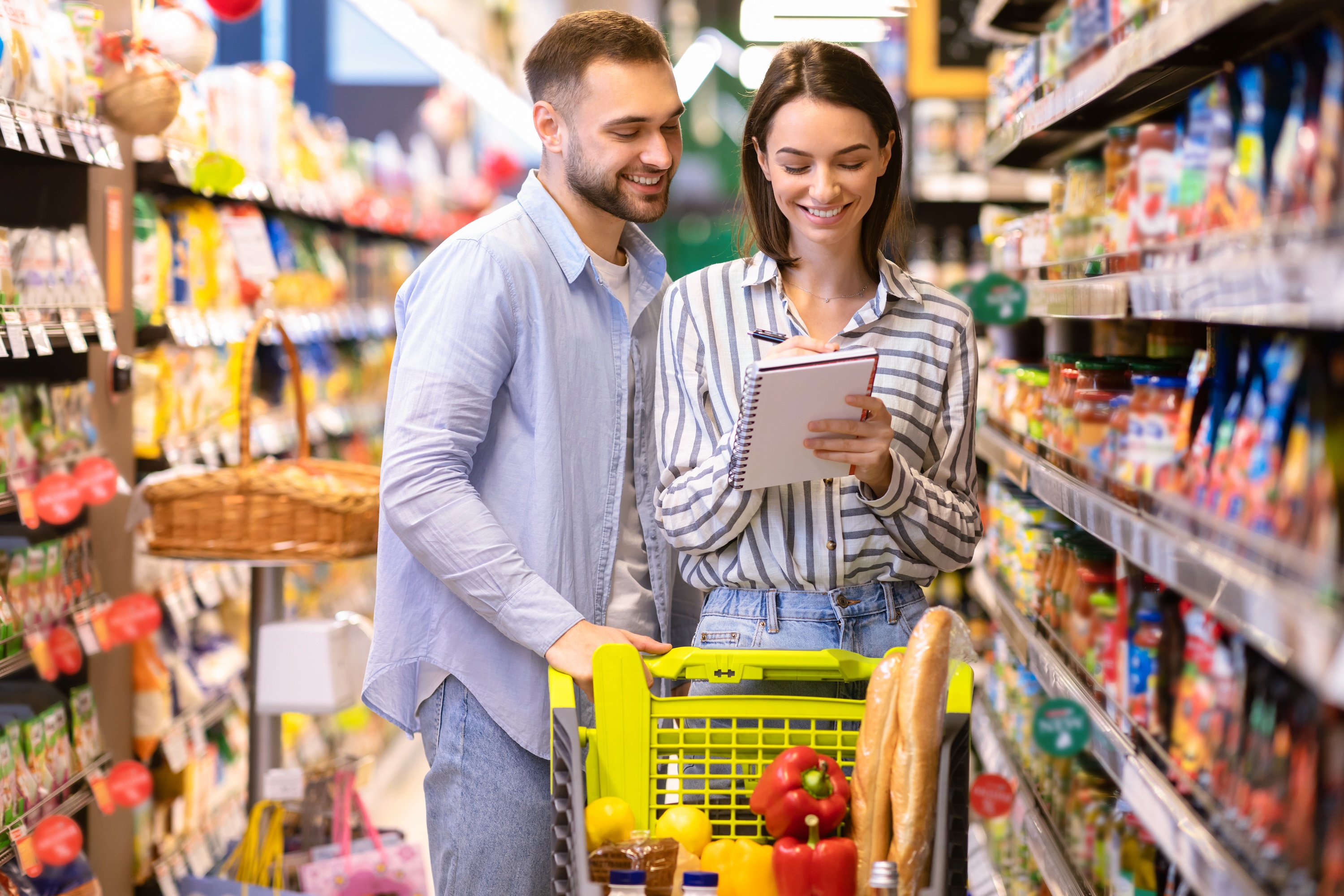Retrato de dos clientes felices sosteniendo lista de compras de supermercado.
