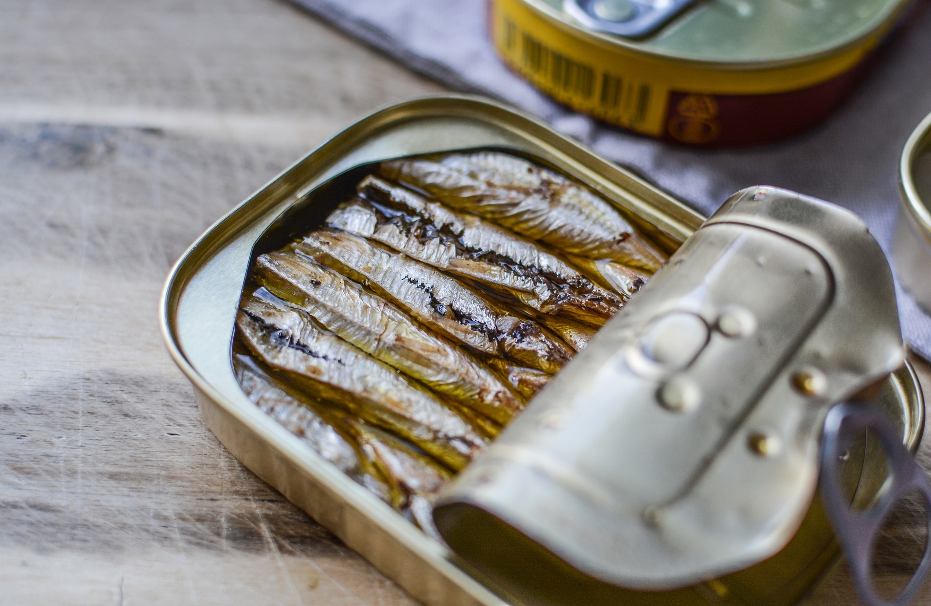 Lata de sardinas medio abierta en aceite sobre una mesa de madera