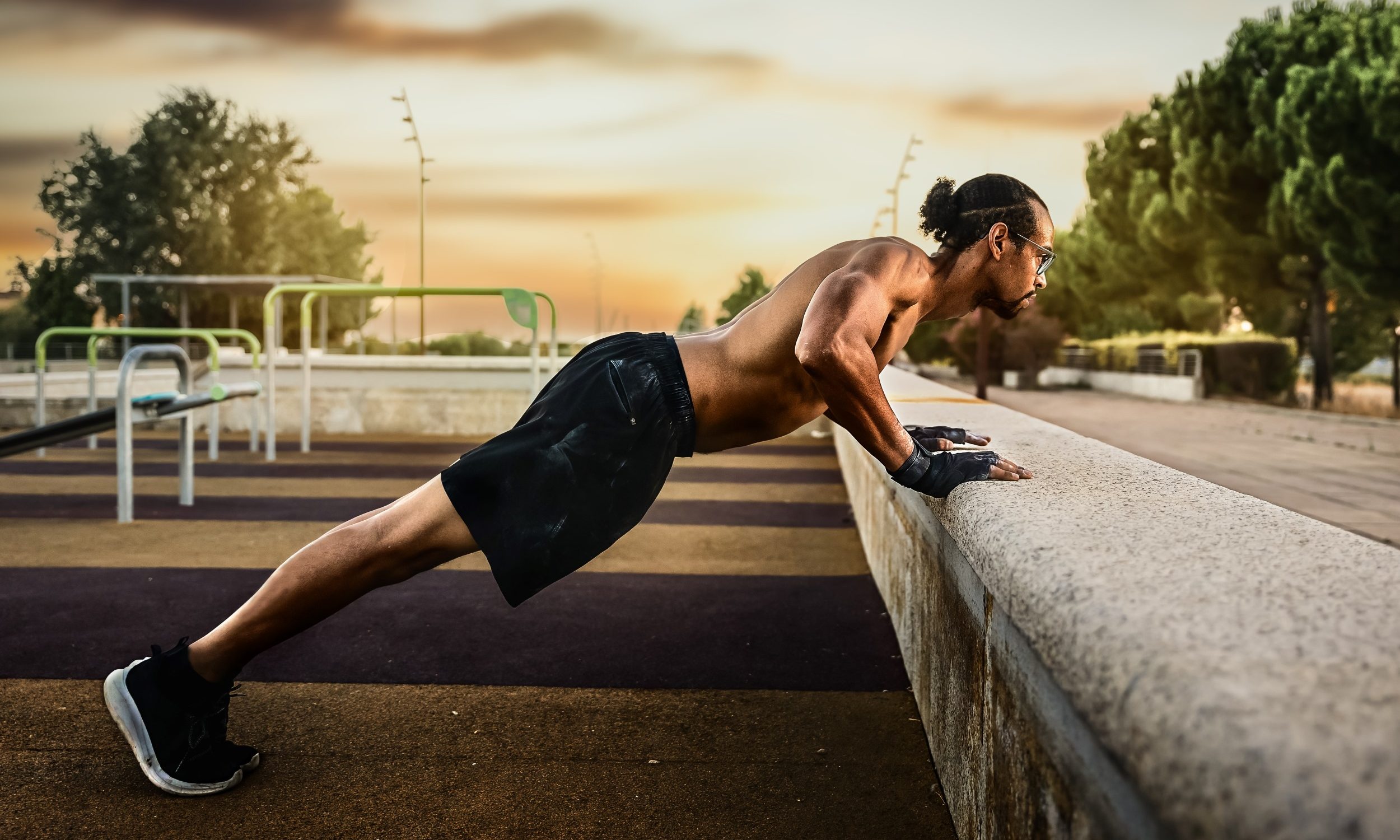 hombre sin camiseta fuera al atardecer haciendo flexiones inclinadas en la pared.